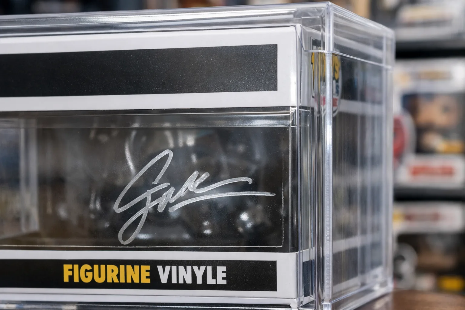 Boîte de figurine signée placée dans une protection transparente, avec l’autographe visible sur le carton.